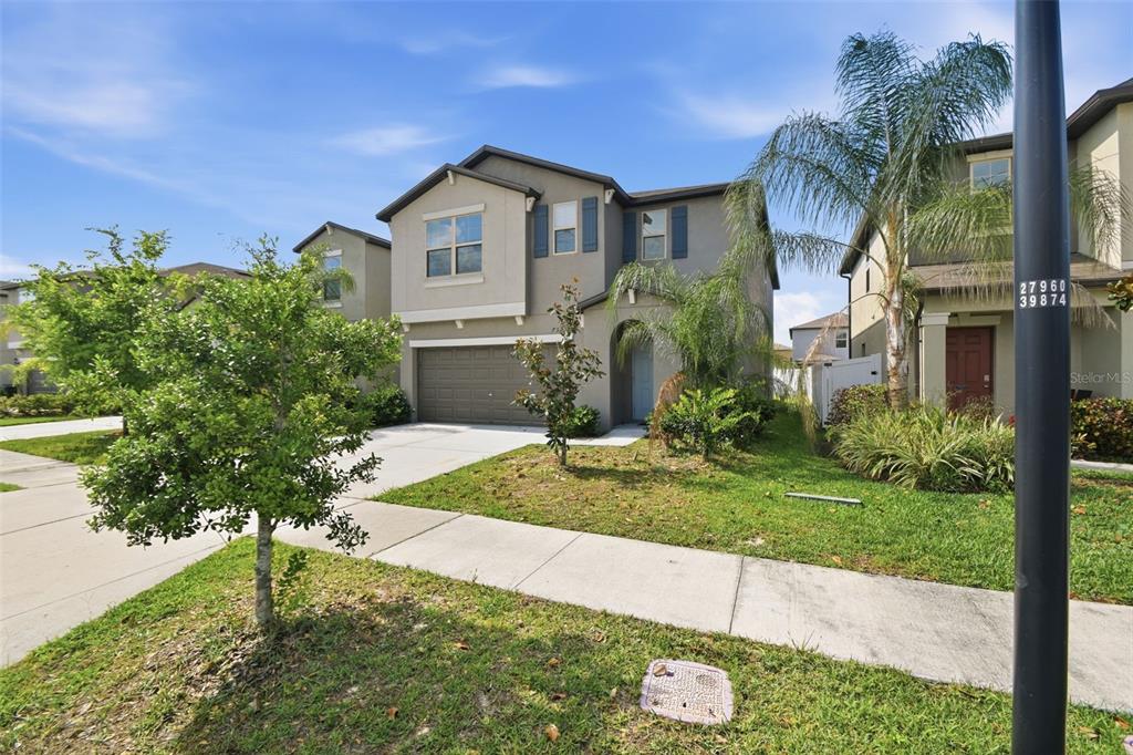 A two-story suburban house with a tan stucco exterior, a two-car garage, and palm trees — 7329 CANTERBURY BELLS COURT, TAMPA, FL