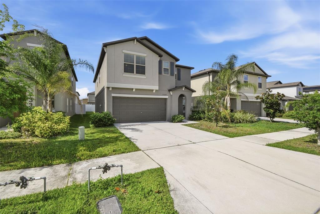 A two-story suburban house with a gray garage and driveway under a blue sky — 7329 CANTERBURY BELLS COURT, TAMPA, FL