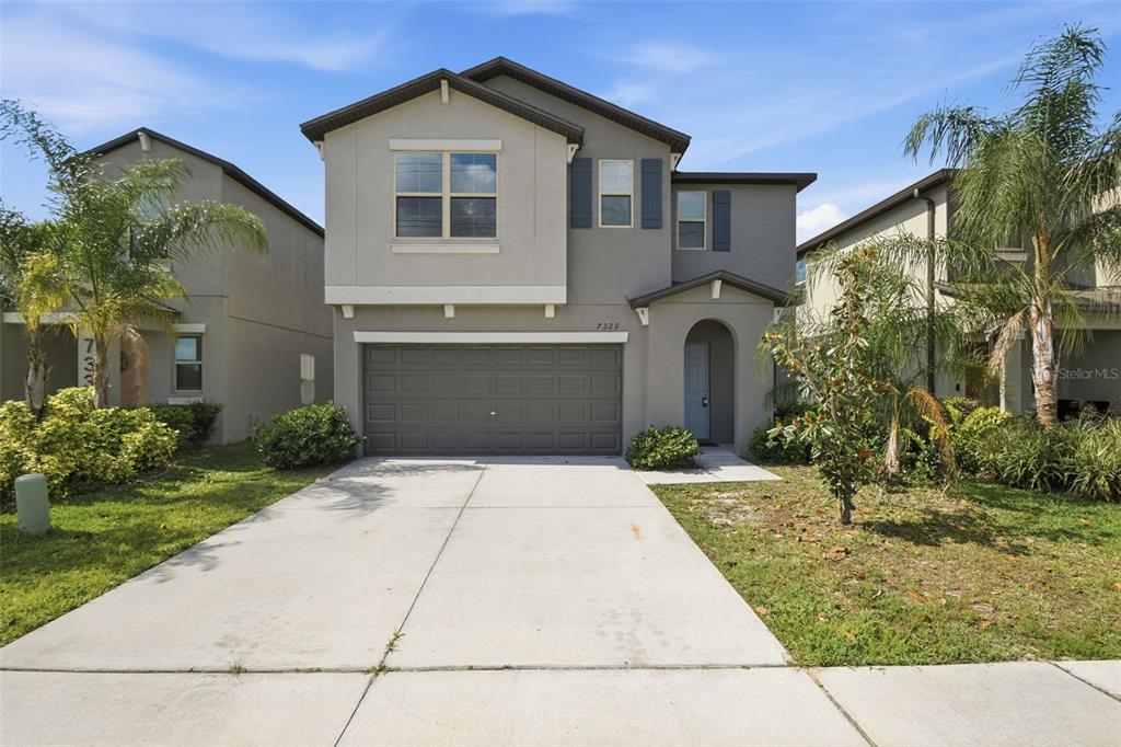 A two-story suburban house with a gray stucco exterior, a two-car garage, and palm trees — 7329 CANTERBURY BELLS COURT, TAMPA, FL