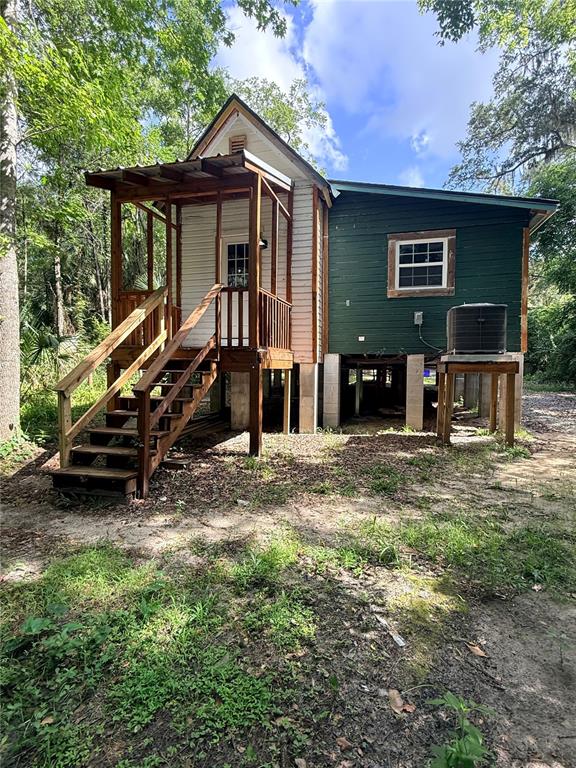 A small, elevated house with a wooden porch, stairs, and green siding sits in a wooded area — 1229 NE 3RD  AVENUE, GAINESVILLE, FL