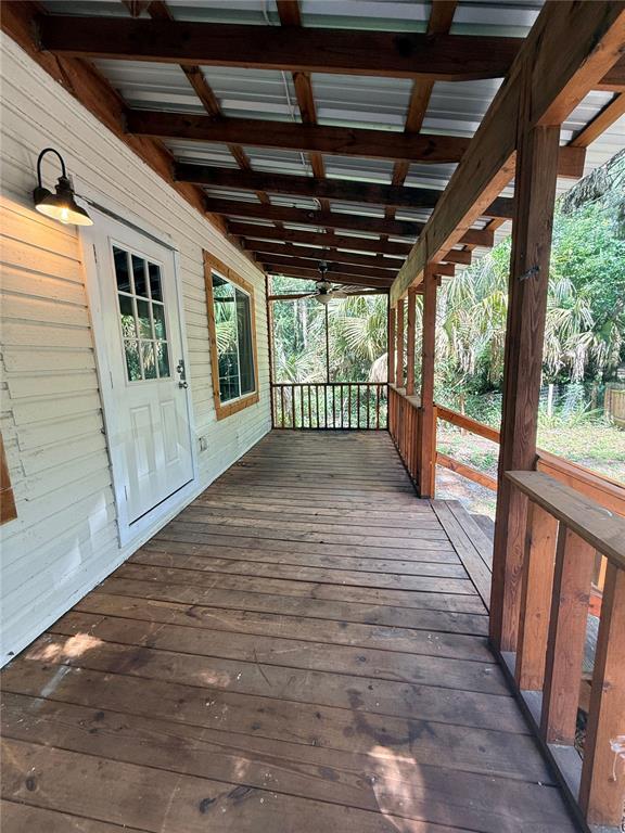 A wooden porch with a metal roof, ceiling fan, and railing overlooks a wooded yard — 1229 NE 3RD  AVENUE, GAINESVILLE, FL