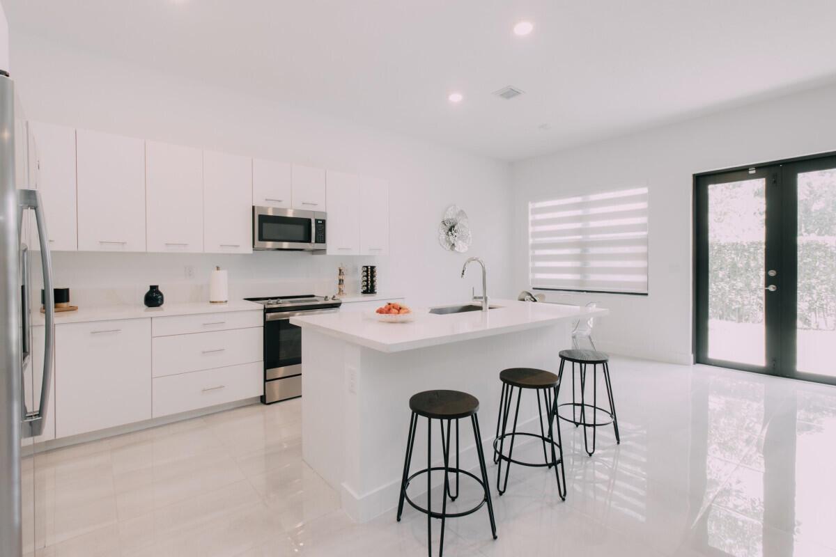 A modern white kitchen features a central island, stainless steel appliances, and three bar stools — 17451 SW 41st Street, Miramar FL 33029, MIRAMAR, FL