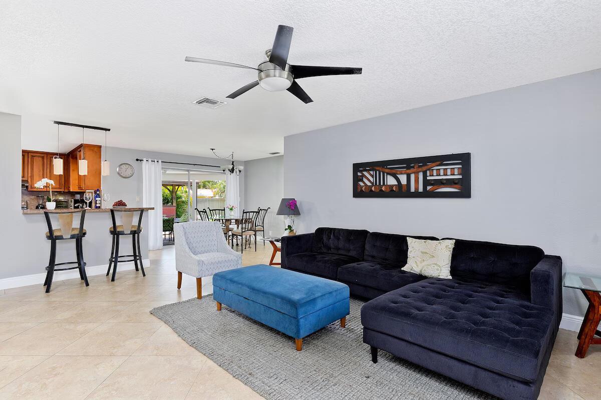 A living room with a black sectional sofa, blue ottoman, and an open-concept kitchen — 4348 NW 2nd Terrace, Boca Raton FL 33431, BOCA RATON, FL