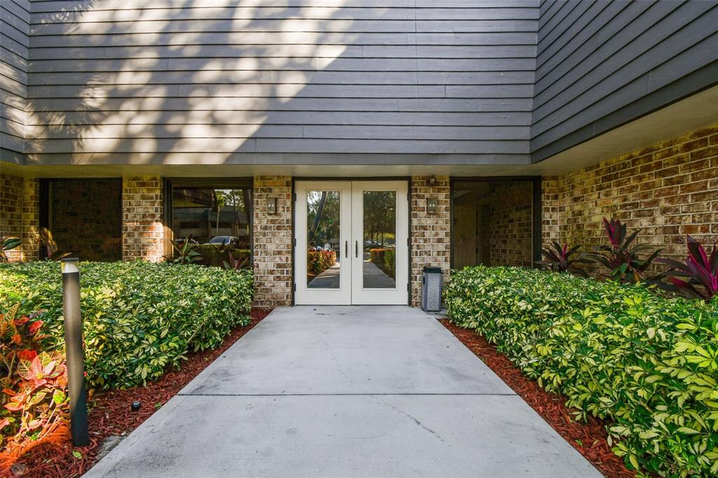 A concrete walkway leads to a double glass door entrance flanked by brick walls — 36750 US HIGHWAY 19 N UNIT 08111, PALM HARBOR, FL