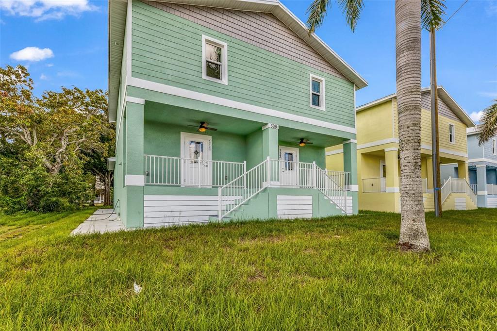 A two-story green house with a covered porch and white railings stands on a lawn — 309 E VIRGINIA AVENUE, PUNTA GORDA, FL
