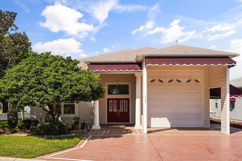 A single-story house exterior features a red front door, a garage, and a large tree — 1075 MOTORCOACH DRIVE, POLK CITY, FL