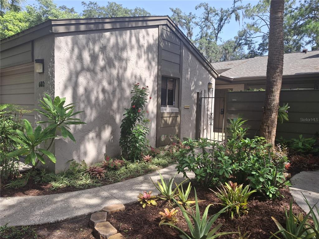A concrete walkway leads to the gated entrance of a single-story home with stucco siding — 602 WOODRIDGE DRIVE, CASSELBERRY, FL