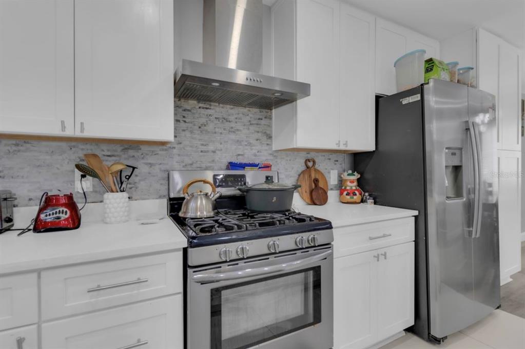 A modern kitchen features a white waterfall island with bar stools and stainless steel appliances — 4849 EDEN VIEW COURT, ORLANDO, FL