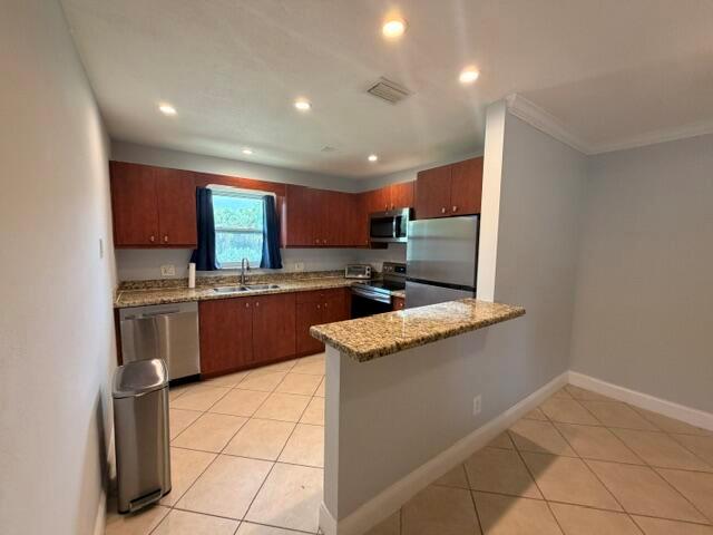 A kitchen features wood cabinets, stainless steel appliances, granite countertops, and light-colored tile flooring — 1983 Juno Road, North Palm Beach FL 33408, NORTH PALM BEACH, FL
