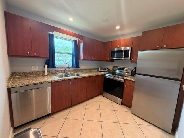 A kitchen features wood cabinets, granite countertops, stainless steel appliances, and beige tile flooring — 1983 Juno Road, North Palm Beach FL 33408, NORTH PALM BEACH, FL