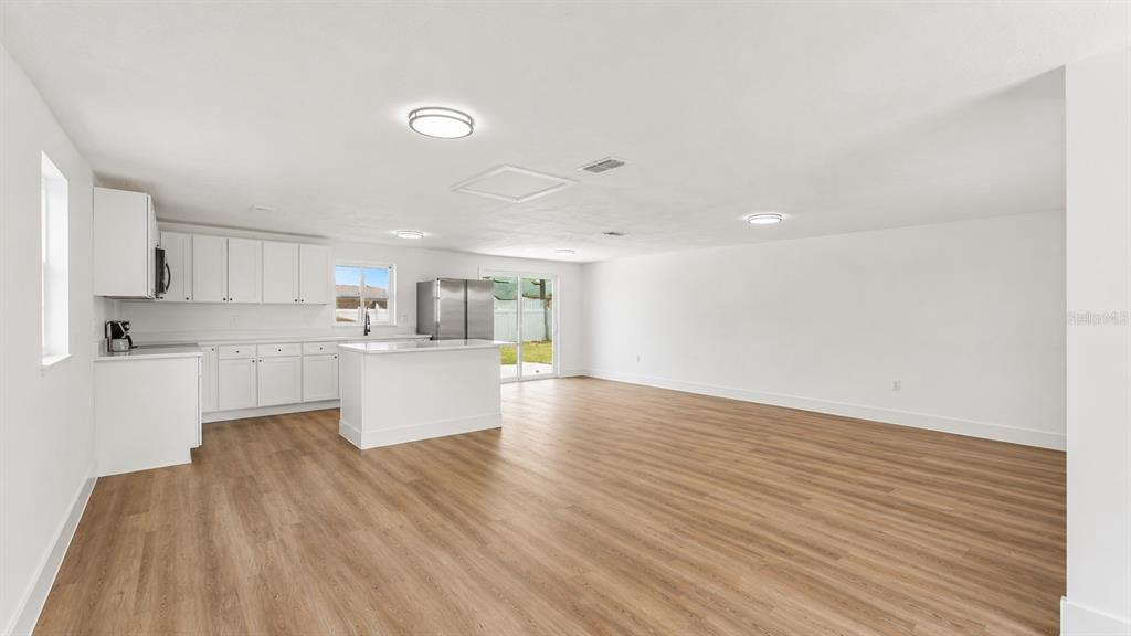 A bright, open-concept kitchen and living area features white cabinetry, an island, and wood flooring — 1726 CORDOVA CIRCLE W, LAKELAND, FL