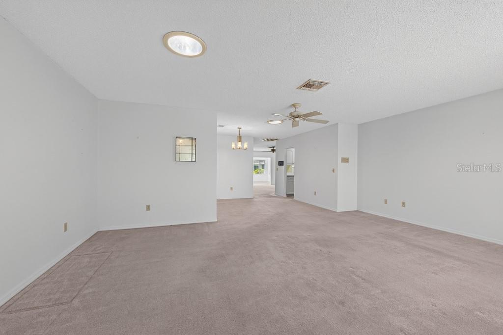 A spacious, carpeted living room with white walls, a ceiling fan, and recessed lighting — 106 SILVERBELL COURT, SUN CITY CENTER, FL