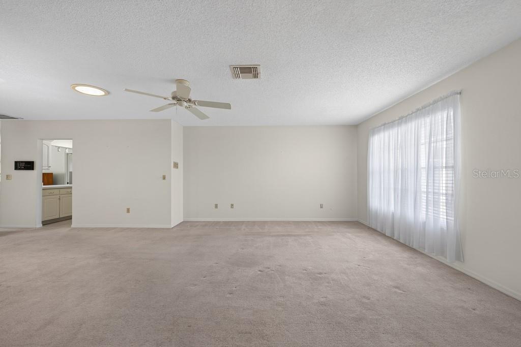A spacious, carpeted living room features white walls, a ceiling fan, and a large window — 106 SILVERBELL COURT, SUN CITY CENTER, FL