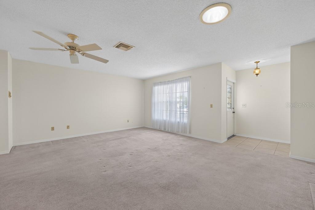 A spacious living room features beige carpeting, white walls, a ceiling fan, and a window — 106 SILVERBELL COURT, SUN CITY CENTER, FL