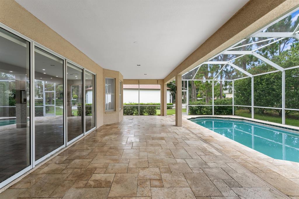 A covered patio with stone flooring overlooks a swimming pool enclosed by a screen cage — 10411 CANARY ISLE DRIVE, TAMPA, FL
