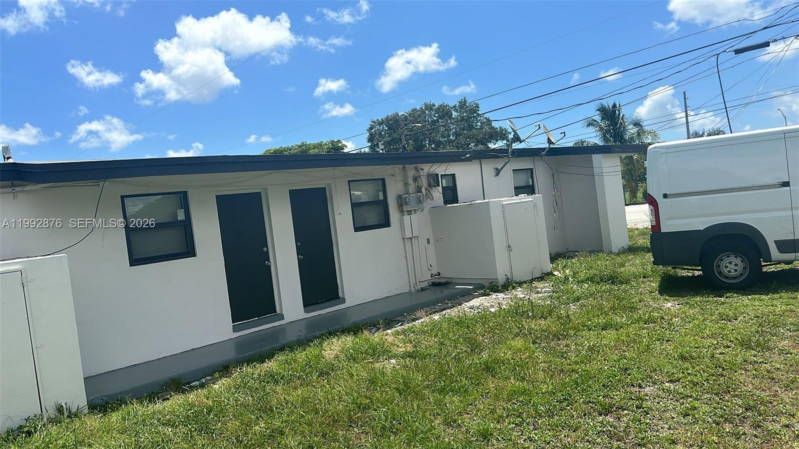 The exterior of a white building features two dark doors, several windows, and a parked van — 2005 Ali Baba Ave, Opa-Locka FL 33054, OPA-LOCKA, FL