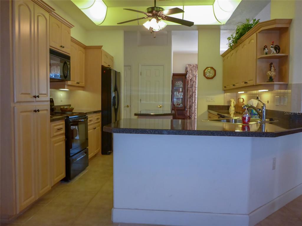 A kitchen features light wood cabinets, black appliances, a dark countertop, and a ceiling fan — 12271 CENTRALIA RD, WEEKI WACHEE, FL