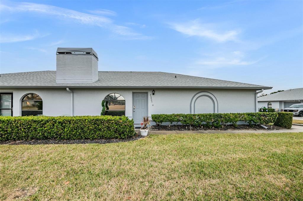A single-story house exterior features a gray facade, a chimney, and a manicured hedge — 23205 CLUB VILLAS DRIVE UNIT 30, LAND O LAKES, FL