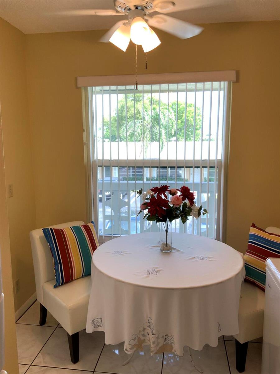 A dining nook features a round table, two white chairs, and a window with blinds — 1121 Cactus Terrace # 202, Delray Beach FL 33445, DELRAY BEACH, FL