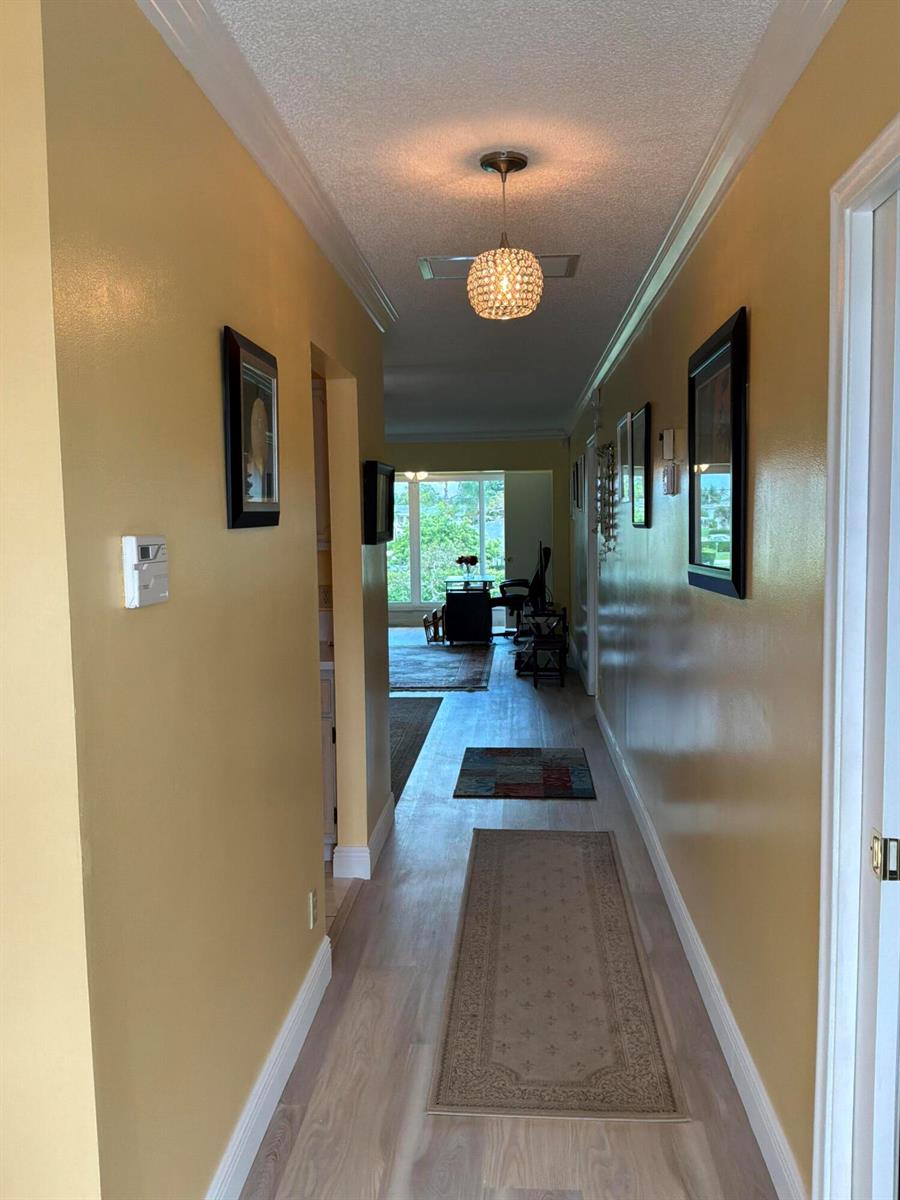 A hallway with yellow walls, light wood-look flooring, and a crystal pendant light fixture — 1121 Cactus Terrace # 202, Delray Beach FL 33445, DELRAY BEACH, FL