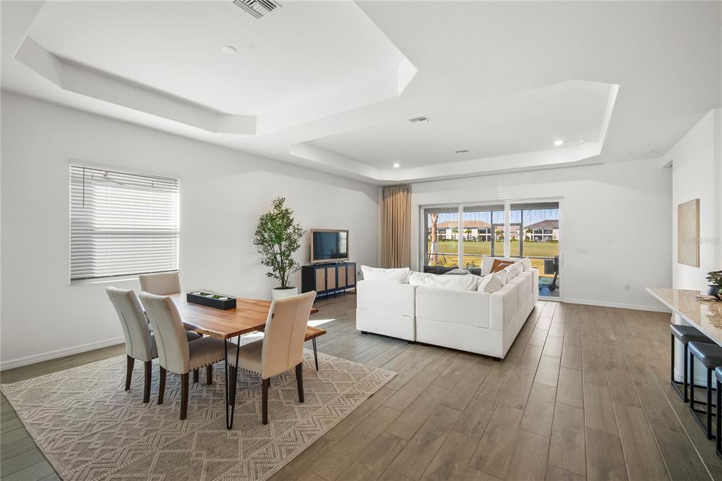 An open-concept living and dining area features a tray ceiling, tile floors, and sliding doors — 15916 N SUGAR HILL DRIVE, PUNTA GORDA, FL