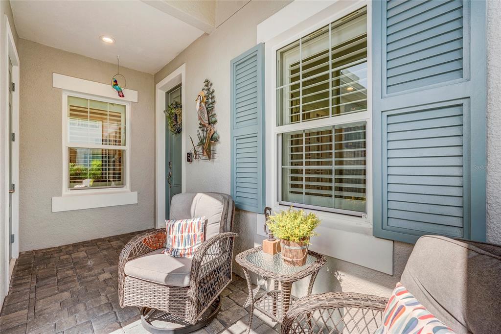 A covered porch features wicker chairs, a small glass table, and blue window shutters — 10233 LAKE WALES CIRCLE, SARASOTA, FL