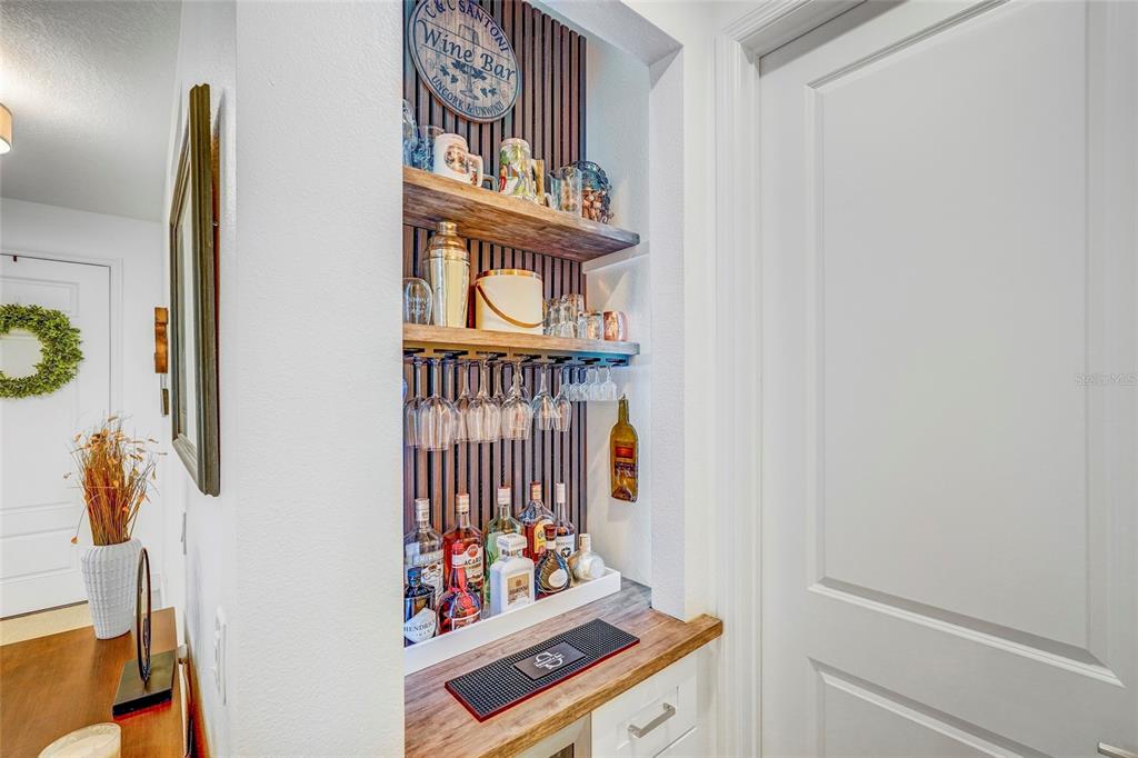 A built-in home bar features wooden shelves, a slatted accent wall, and hanging glassware — 10233 LAKE WALES CIRCLE, SARASOTA, FL
