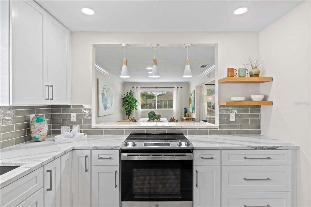 A kitchen features white cabinets, marble-look countertops, gray subway tile backsplash, and a pass-through window — 2641 MARTIN STREET, SARASOTA, FL