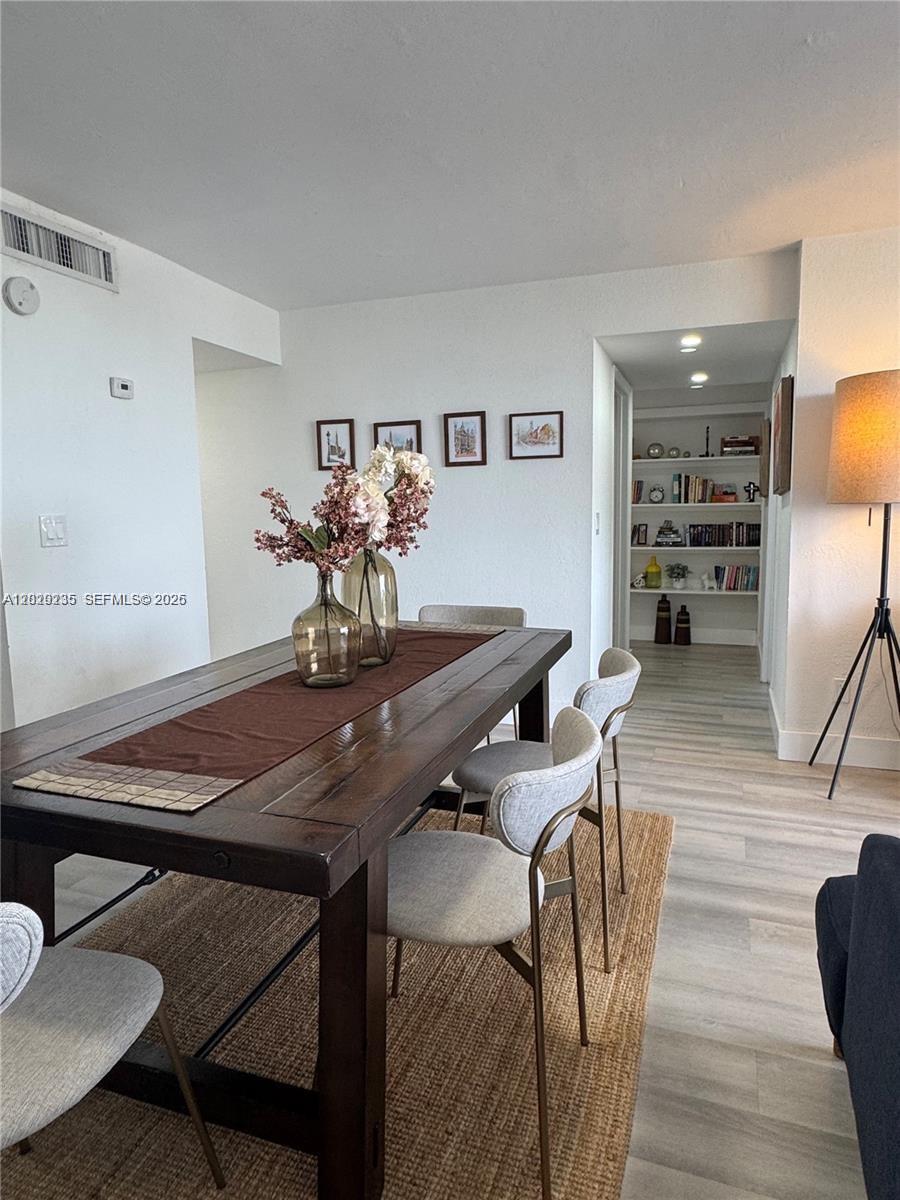 A dining room features a dark wood table, light-colored chairs, and a built-in bookshelf — 2000 NE 135th St # 609, North Miami FL 33181, NORTH MIAMI, FL
