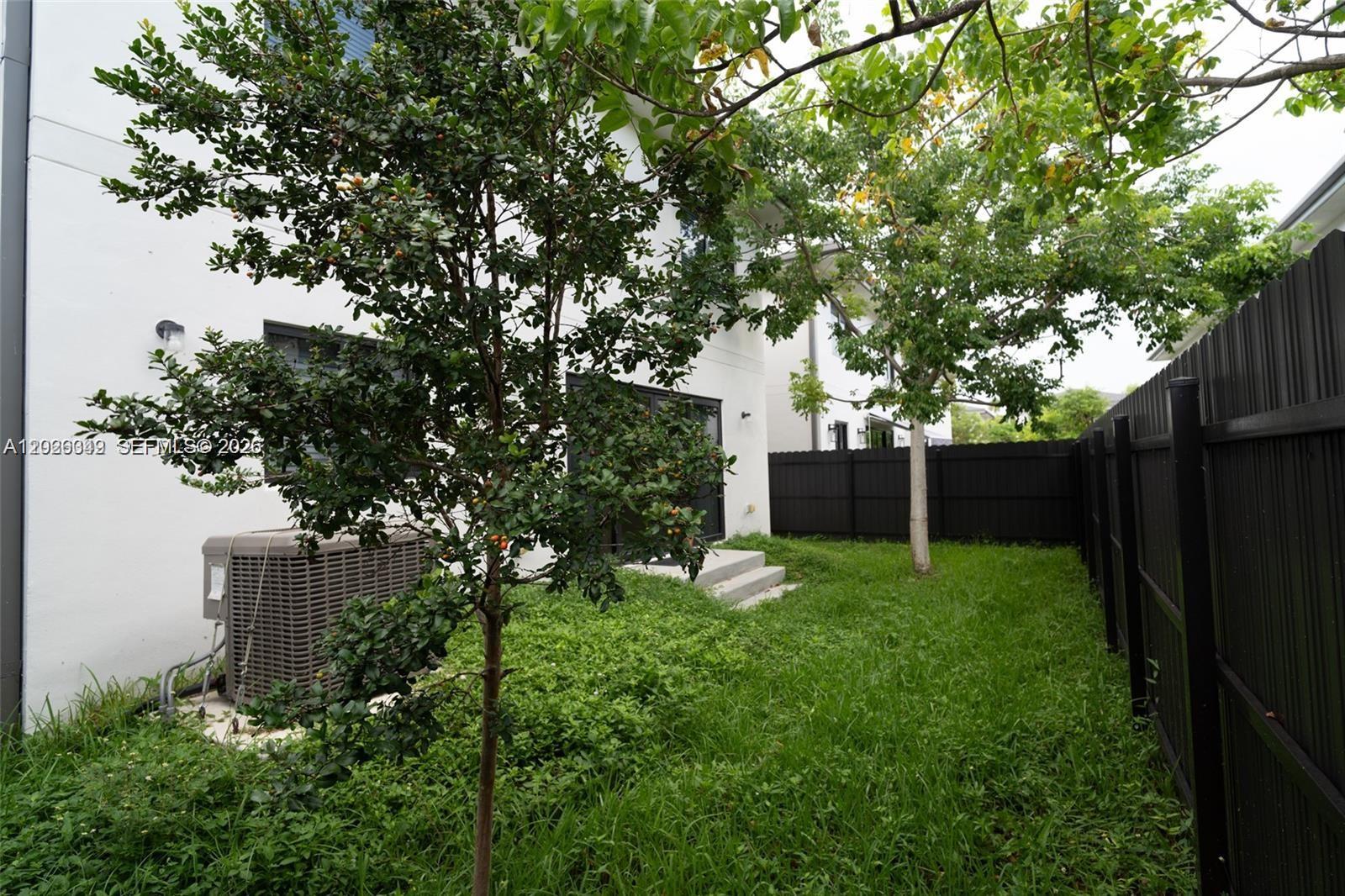 A backyard features a small tree, a central air conditioning unit, and a black fence — 1159 NW 3rd St, Florida City FL 33034, FLORIDA CITY, FL