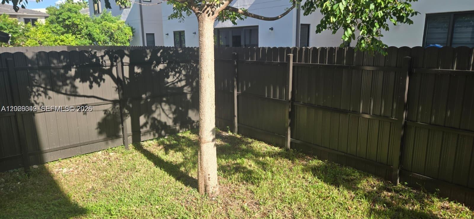 A small grassy backyard features a tree and a tall dark metal privacy fence — 1159 NW 3rd St, Florida City FL 33034, FLORIDA CITY, FL