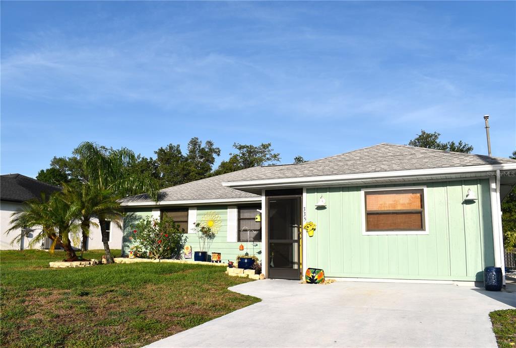 A light green single-story house features a concrete driveway and a screened front entryway — 335 HARBOR BOULEVARD, PORT CHARLOTTE, FL