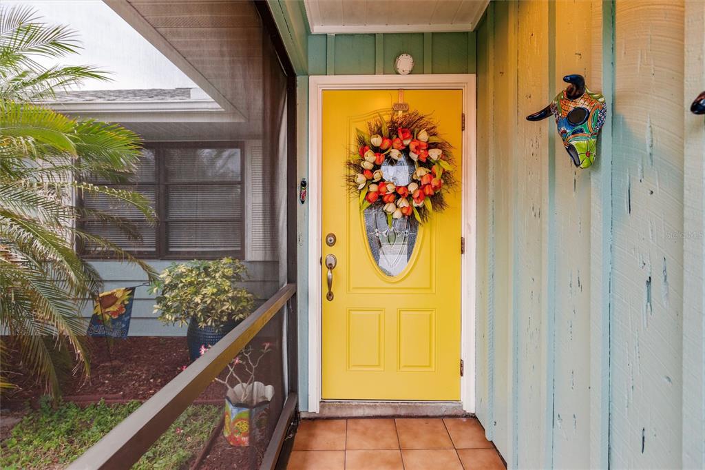 A bright yellow front door with a floral wreath sits on a tiled porch — 335 HARBOR BOULEVARD, PORT CHARLOTTE, FL