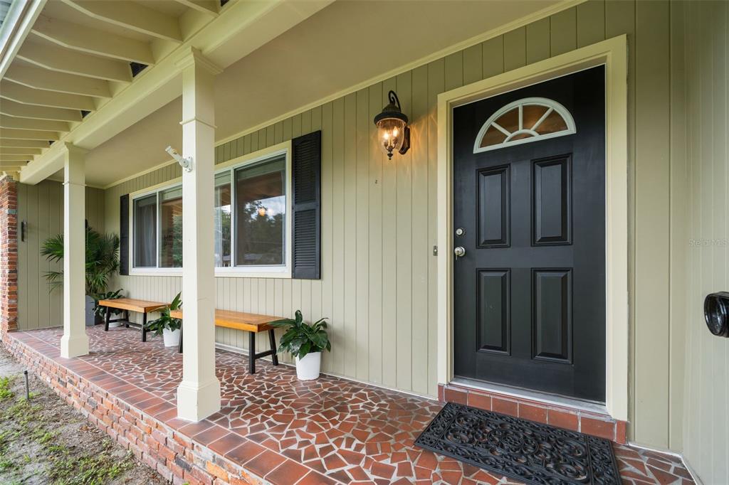 A covered porch with a tiled floor, wooden benches, and a black front door — 817 NW 37TH DRIVE, GAINESVILLE, FL