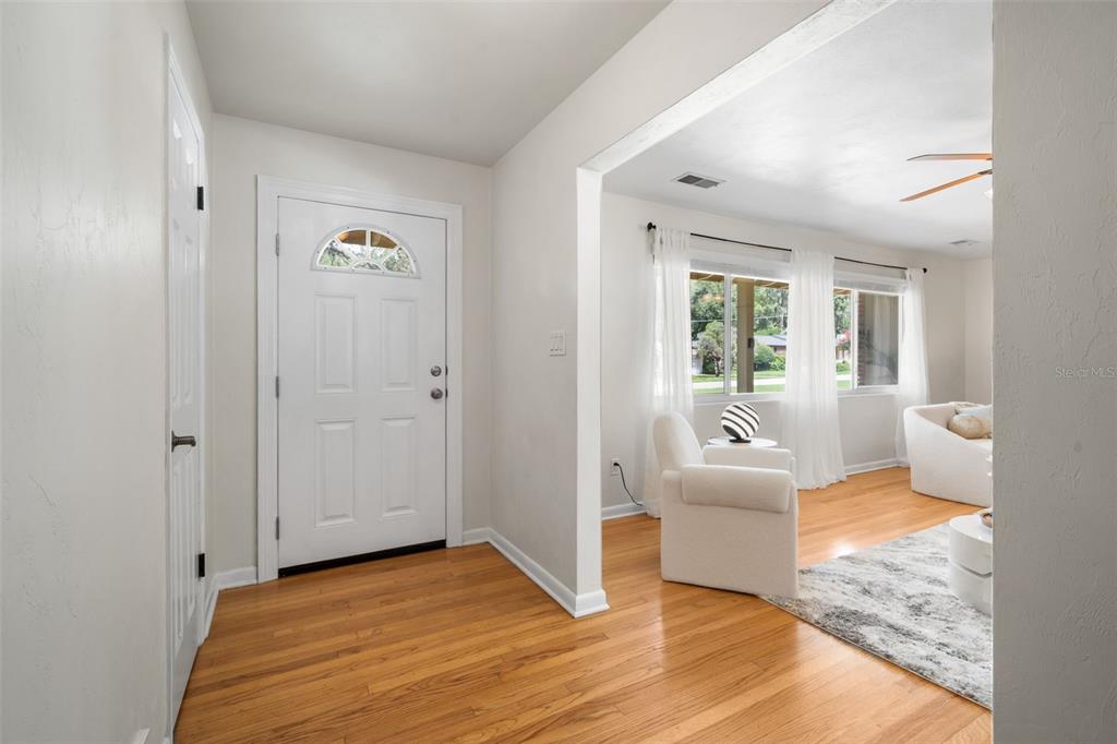 An entryway with hardwood floors leads into a bright living room with white furniture — 817 NW 37TH DRIVE, GAINESVILLE, FL