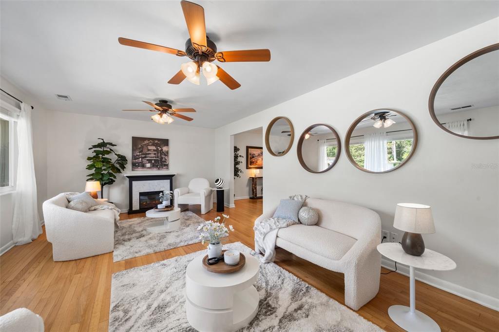 A bright living room features two white sofas, two circular rugs, and three round wall mirrors — 817 NW 37TH DRIVE, GAINESVILLE, FL