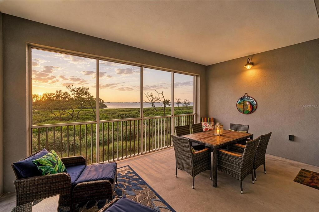 A screened-in patio features wicker furniture and a view of the water at sunset — 392 ARUBA CIRCLE UNIT 102, BRADENTON, FL