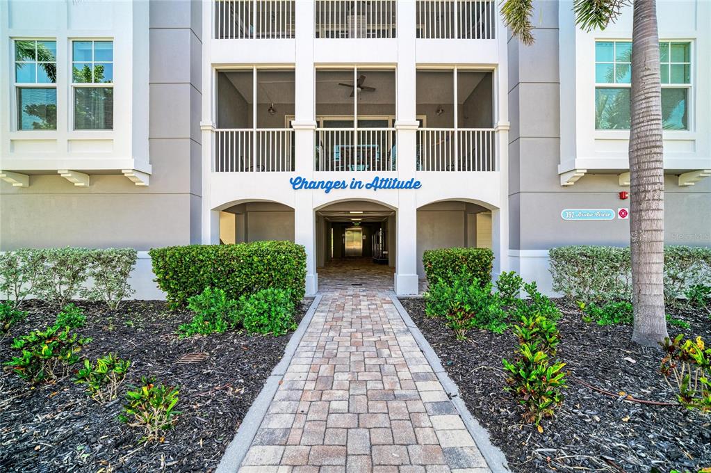 A paved walkway leads to the entrance of a multi-story building with a screened balcony — 392 ARUBA CIRCLE UNIT 102, BRADENTON, FL