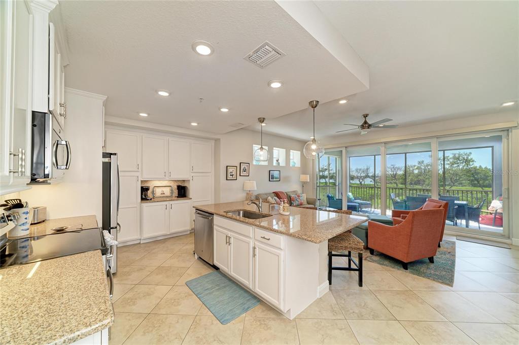 A kitchen with white cabinets and granite countertops opens to a living area and balcony — 392 ARUBA CIRCLE UNIT 102, BRADENTON, FL