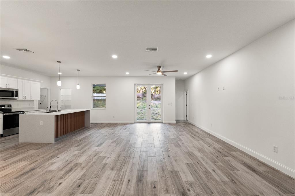 An open-concept kitchen and living area features white cabinetry, a wood-paneled island, and wood-look flooring — 5352 LOWELL AVENUE, SPRING HILL, FL