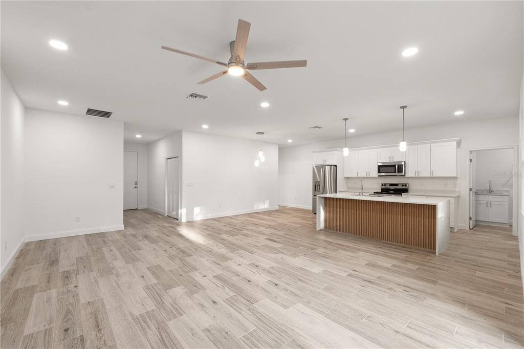 An open-concept kitchen and living area features light wood-look tile flooring and white cabinetry — 5352 LOWELL AVENUE, SPRING HILL, FL