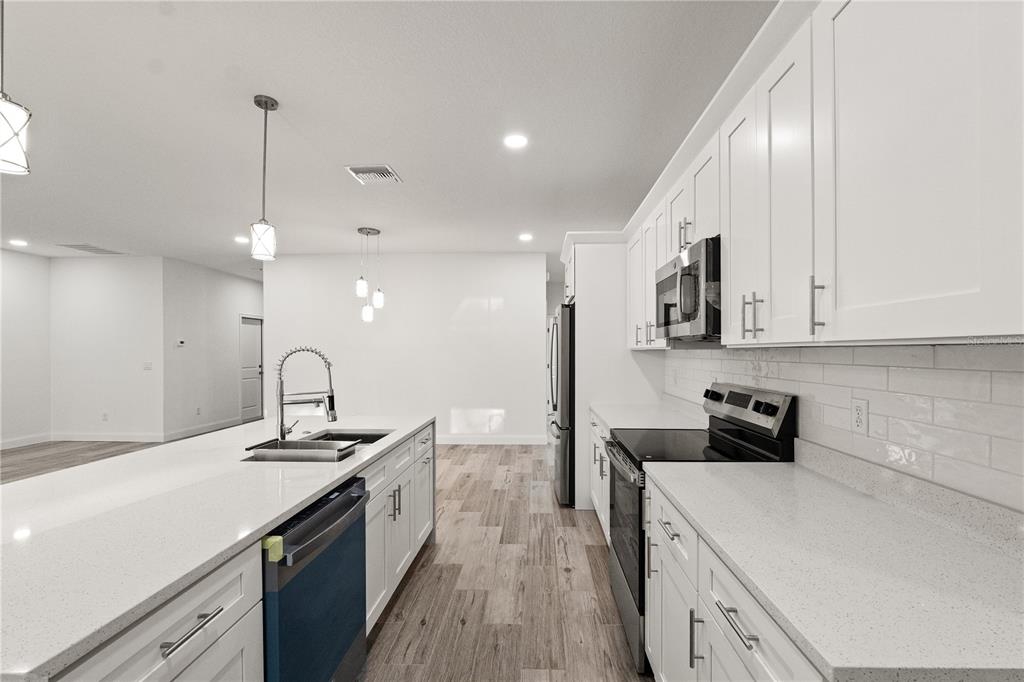 A modern kitchen features white cabinetry, quartz countertops, stainless steel appliances, and wood-look tile flooring — 5352 LOWELL AVENUE, SPRING HILL, FL