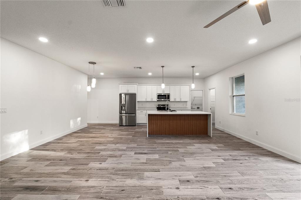 A modern kitchen features white cabinetry, a wood-slatted island, and light-colored wood-look tile flooring — 5352 LOWELL AVENUE, SPRING HILL, FL