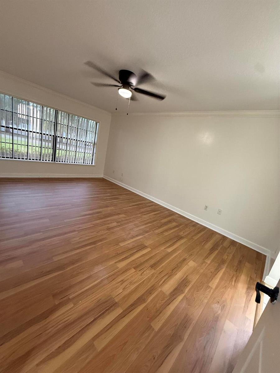 An empty room features light-colored walls, wood-look flooring, a ceiling fan, and a large window — 1723 Mariners Cove # A, Fort Pierce FL 34950, FORT PIERCE, FL