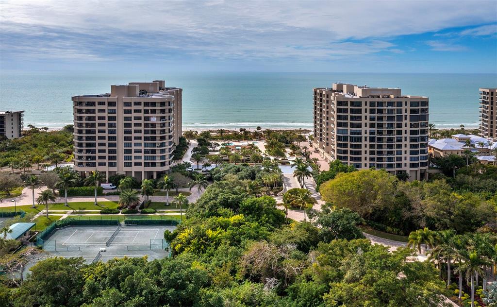 An aerial view shows two large residential buildings near a beach with tennis courts below — 1211 GULF OF MEXICO DRIVE UNIT 709, LONGBOAT KEY, FL