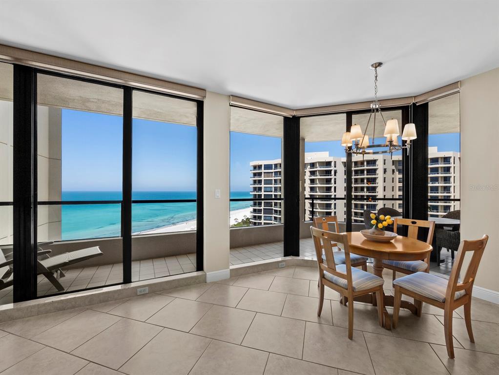 A dining area with tile floors, a wooden table, and floor-to-ceiling windows overlooking the ocean — 1211 GULF OF MEXICO DRIVE UNIT 709, LONGBOAT KEY, FL