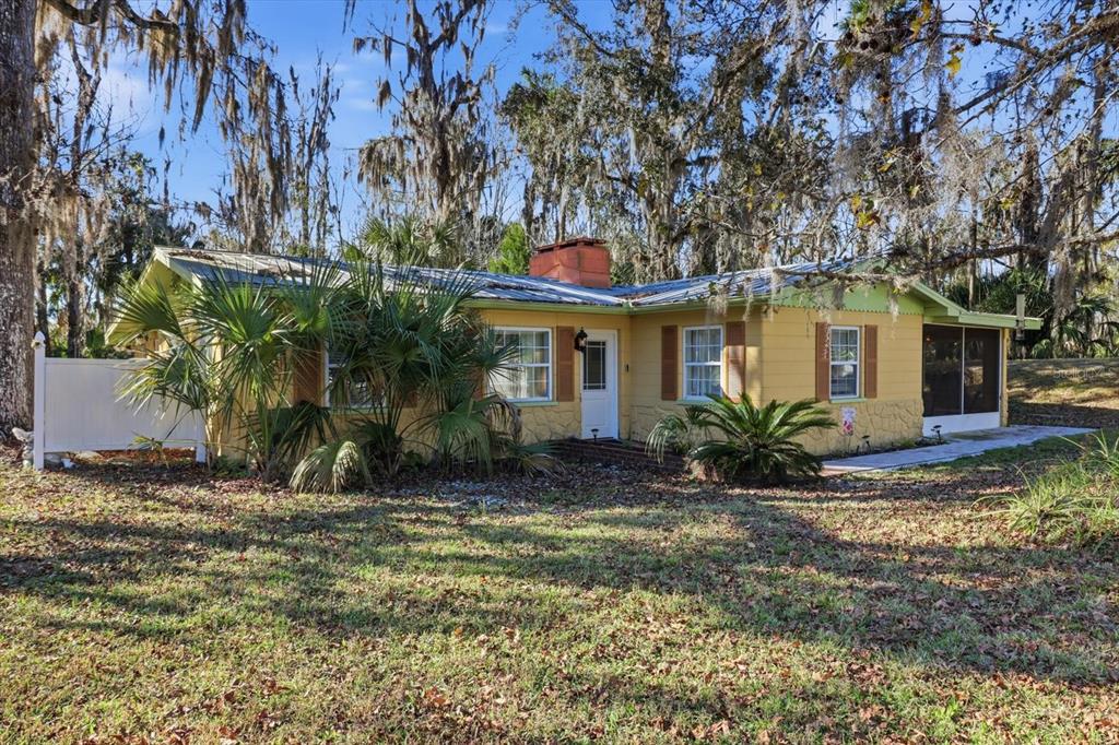 A yellow single-story house with a metal roof, brick chimney, and surrounding trees — 10170 W YULEE DRIVE, HOMOSASSA, FL