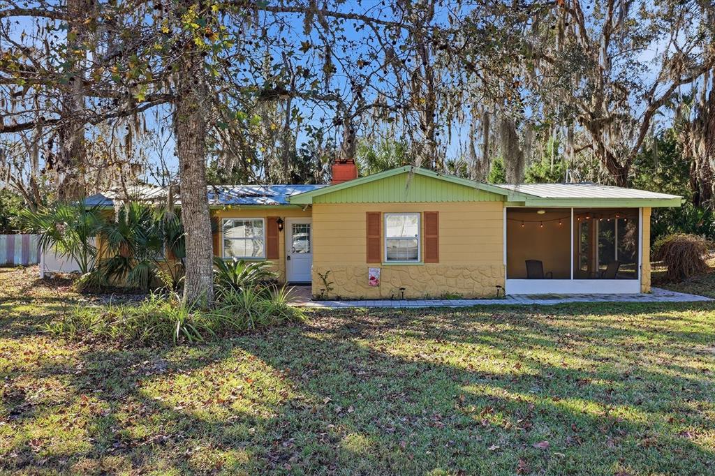 A single-story yellow house with a metal roof and a screened-in porch under trees — 10170 W YULEE DRIVE, HOMOSASSA, FL