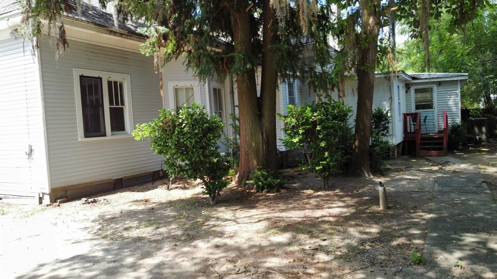 A side view of a light-colored house with large trees and a red wooden staircase — 25 Madison Street, FL 32324, FL