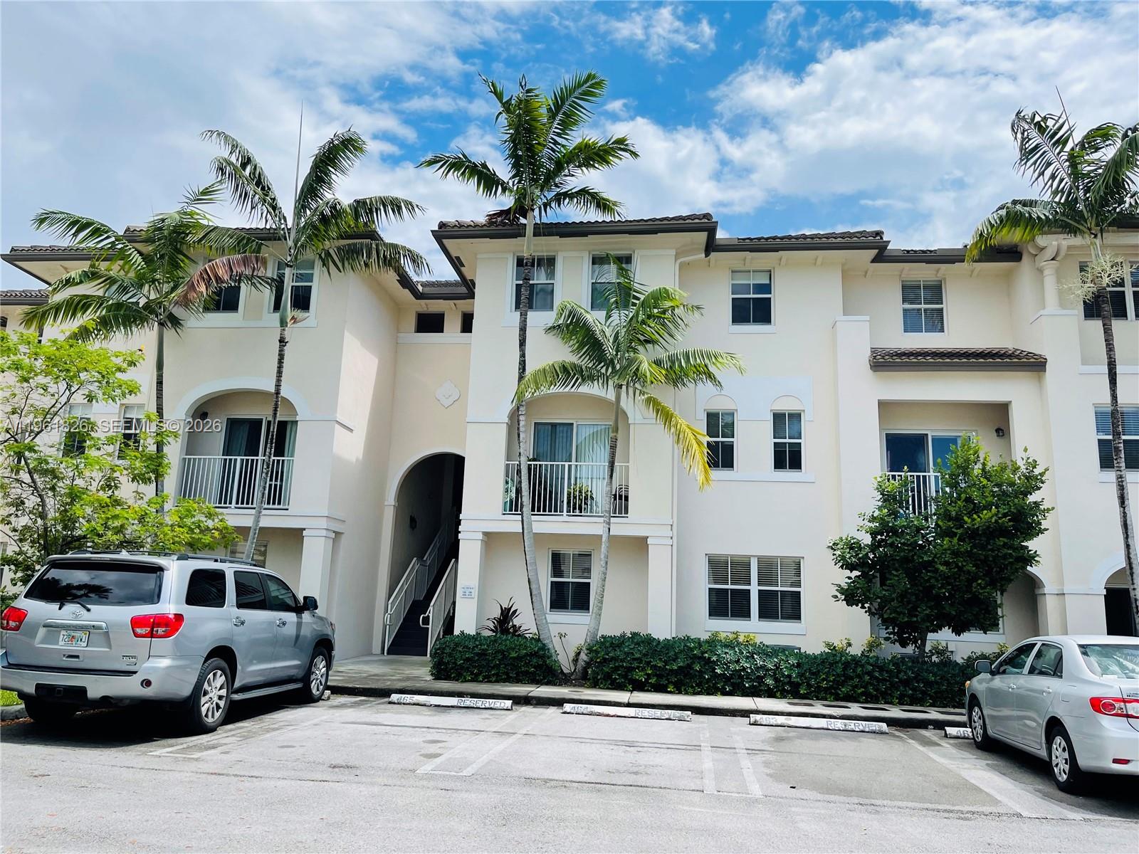 A three-story apartment building with palm trees and parked cars in the foreground — 11601 NW 89th St # 106, Doral FL 33178, DORAL, FL